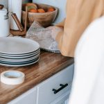 A woman wraps plates in bubble wrap on a kitchen counter, preparing for a move.