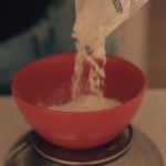 Pouring flour into a red bowl placed on a digital scale for measuring.