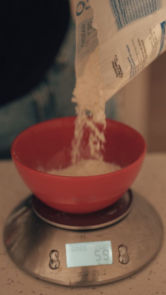Pouring flour into a red bowl placed on a digital scale for measuring.