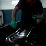 Mechanic in gloves inspecting car engine in a well lit garage setting.