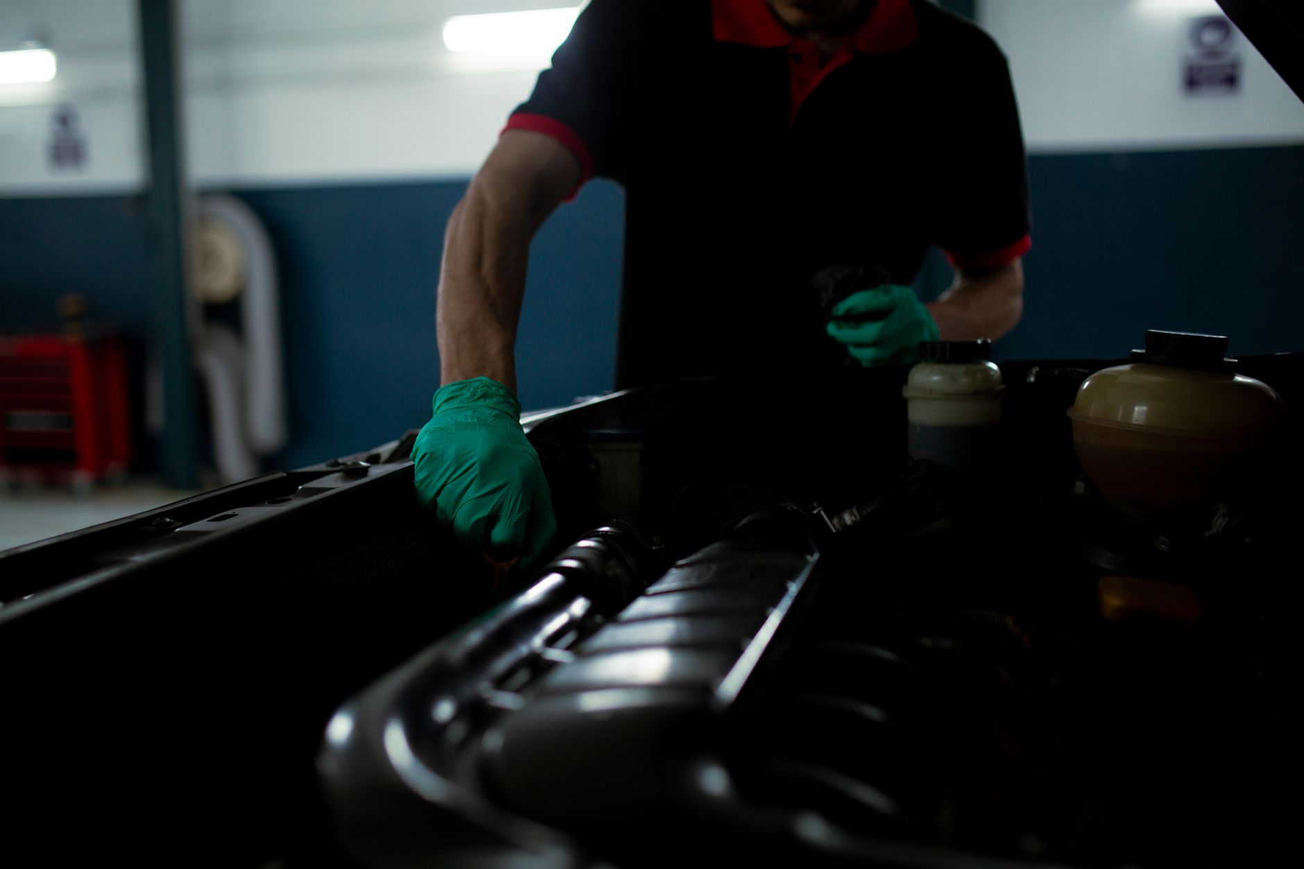 Mechanic in gloves inspecting car engine in a well lit garage setting.