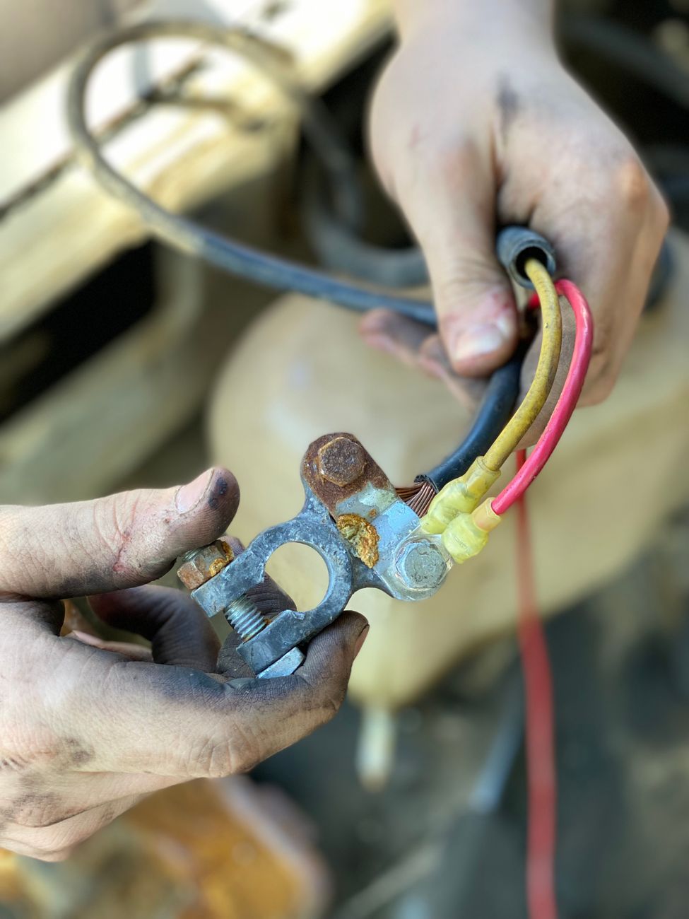 Hands holding a corroded battery terminal with multi colored wires in a repair setting.