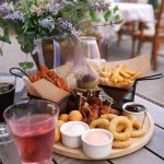 Delicious assortment of fried snacks and sauces on a wooden platter at a charming outdoor restaurant.
