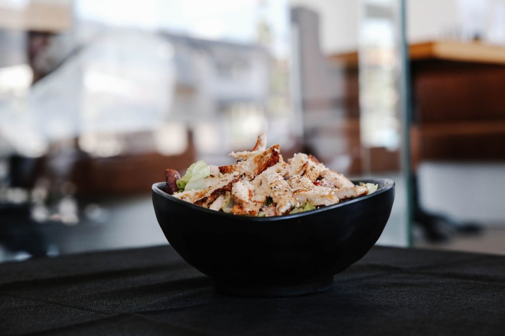Savor this close up of a grilled chicken salad in a stylish black bowl indoors.