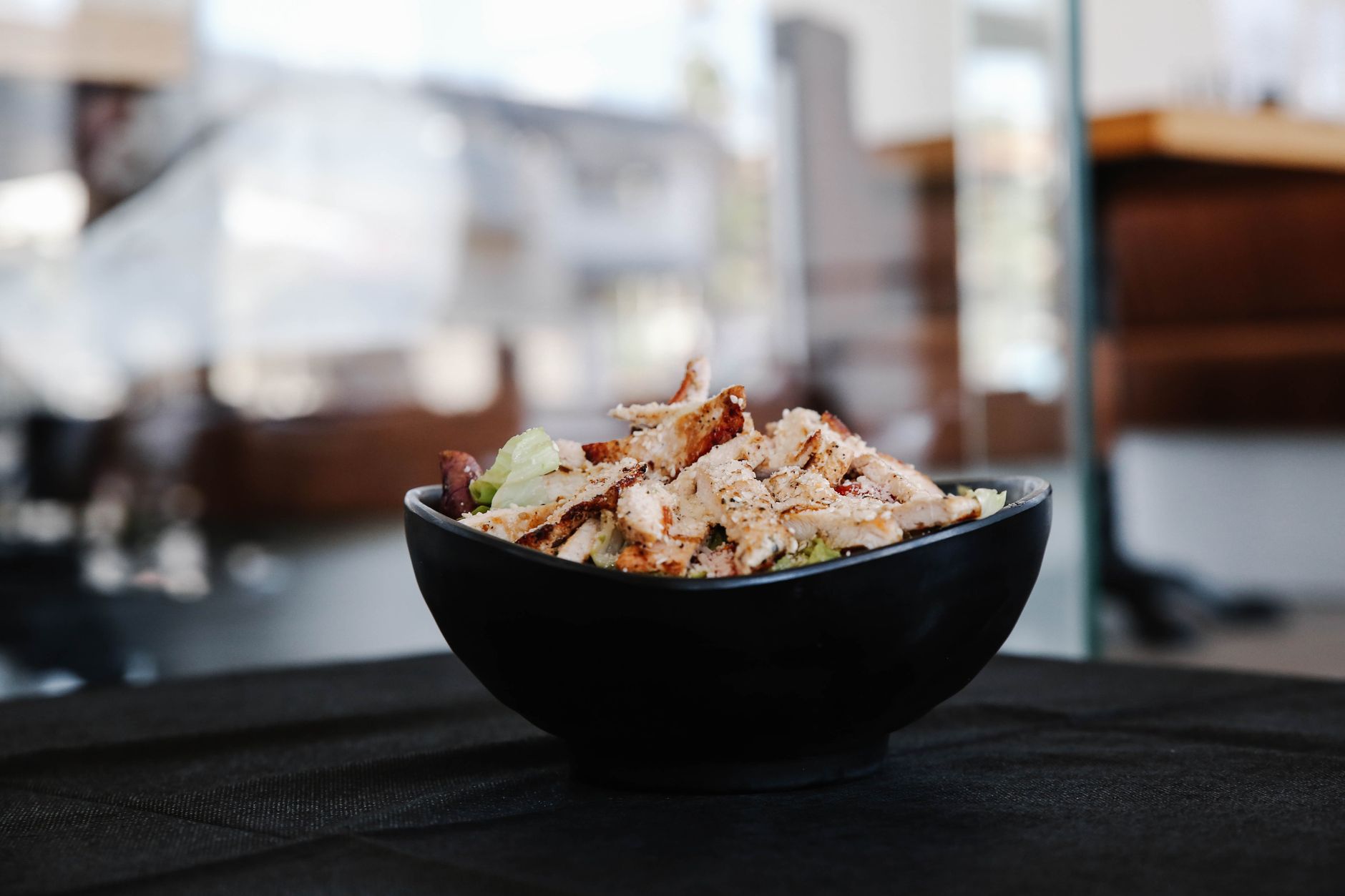 Savor this close up of a grilled chicken salad in a stylish black bowl indoors.