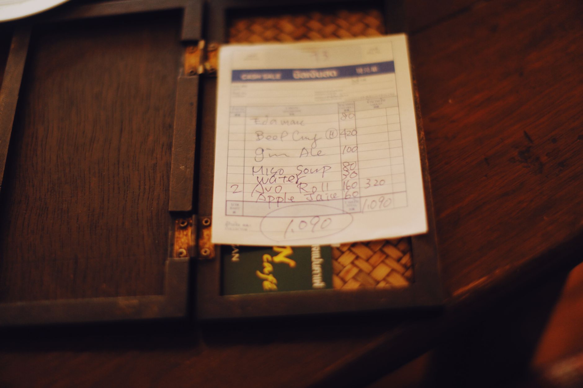 Close up of a restaurant bill placed on a dark wooden table, creating a moody ambiance.