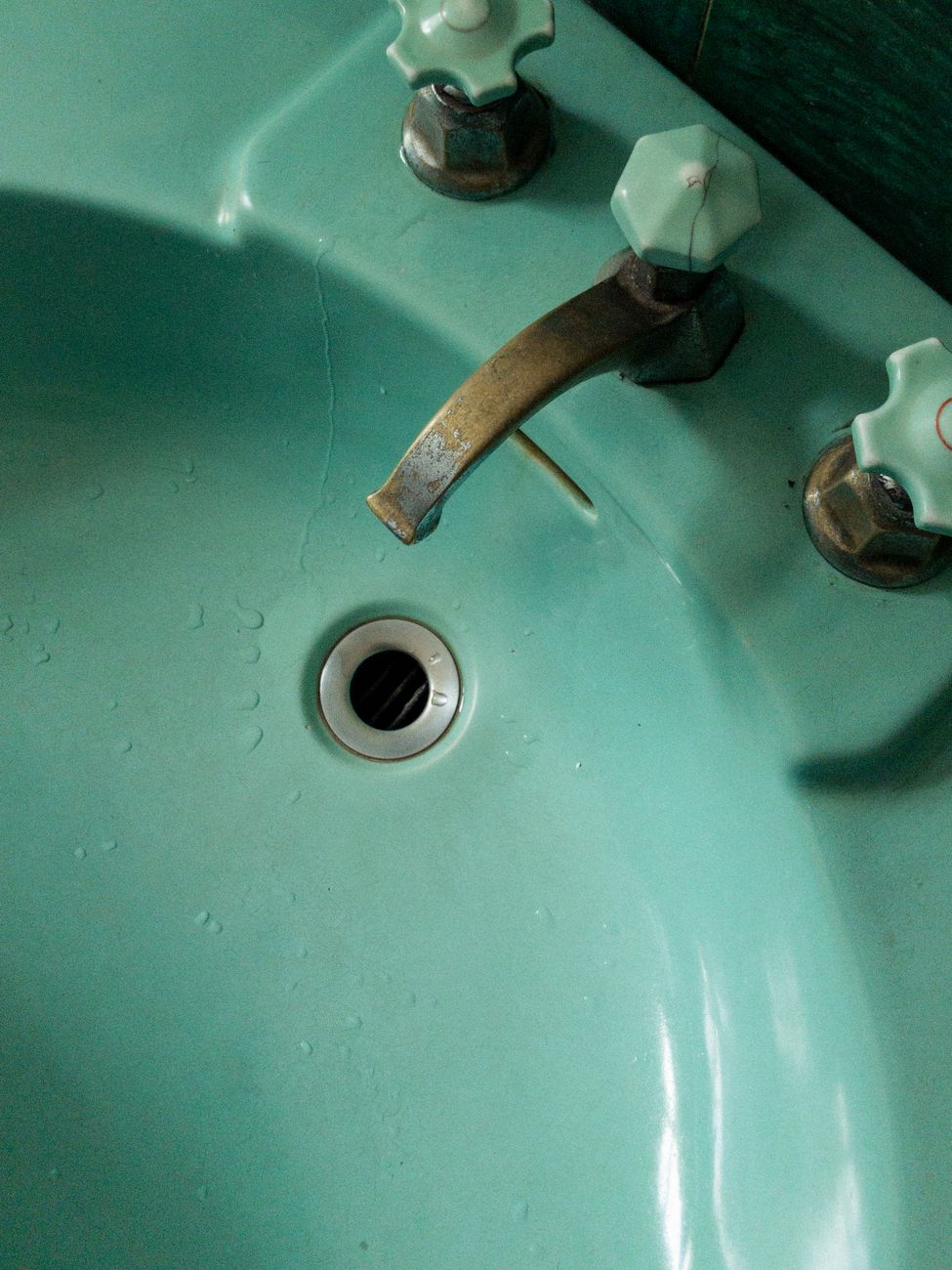 A close up view of a vintage aqua colored sink featuring a rusty faucet and unique decor detailing.
