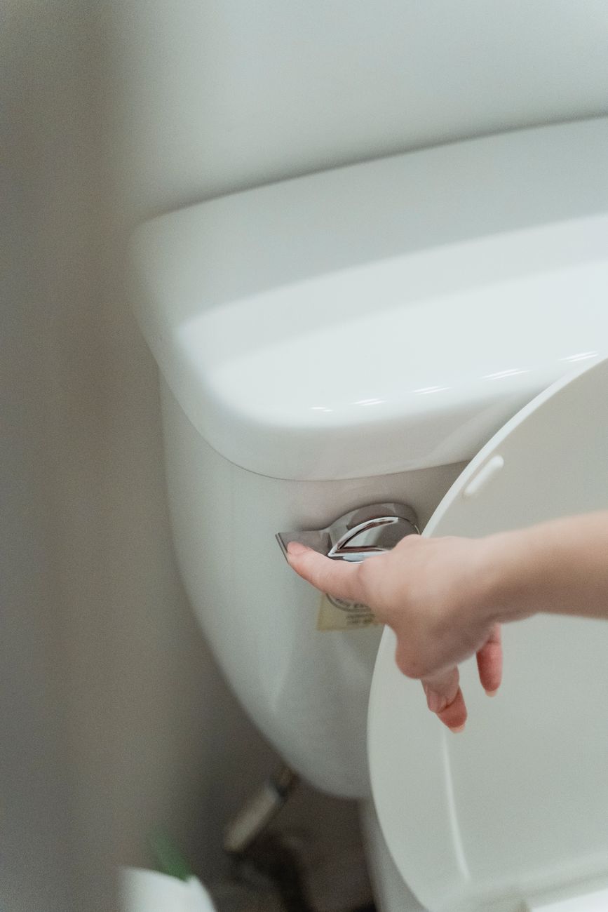 Close up of a hand flushing a modern toilet, emphasizing hygiene and water conservation.
