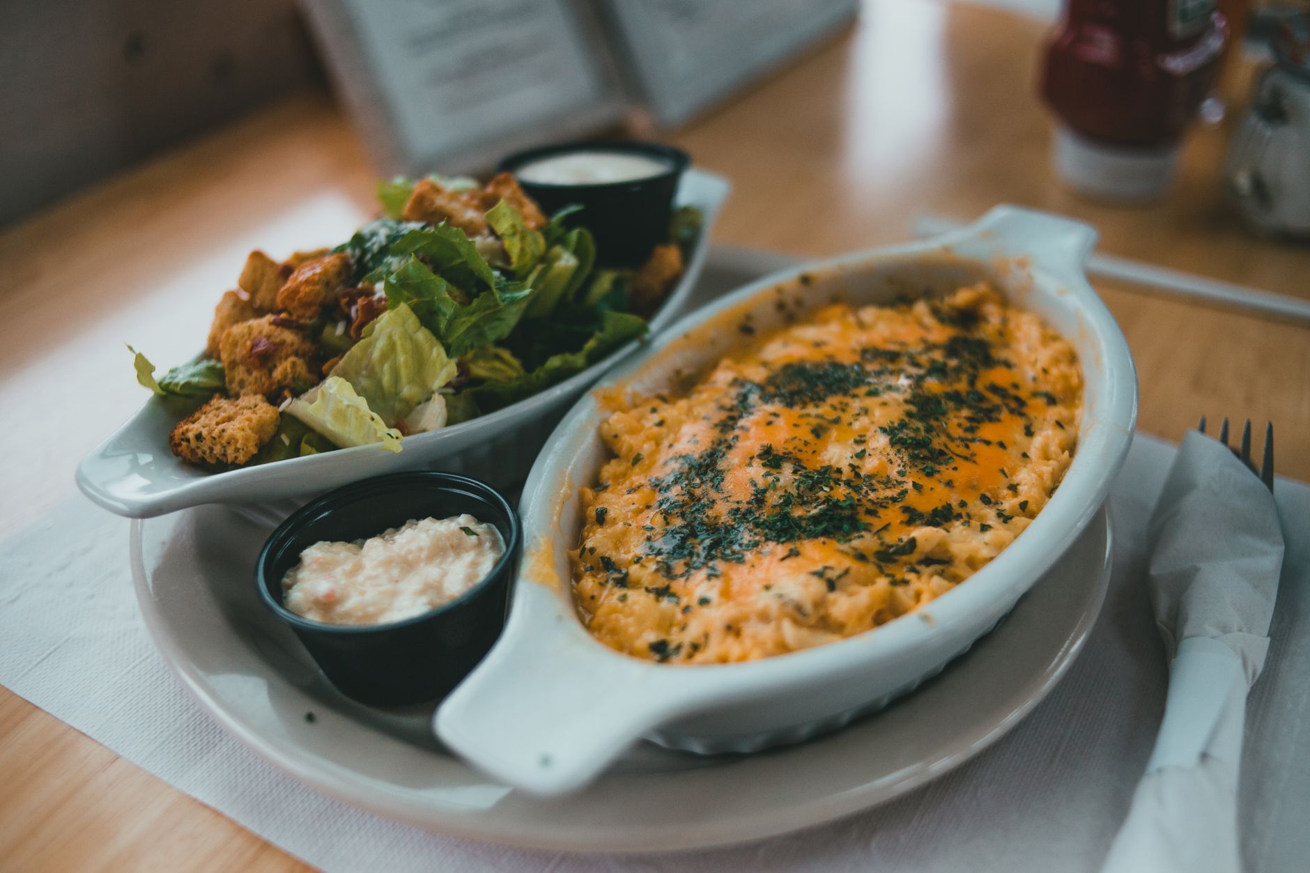 Delicious baked pasta and Caesar salad served indoors, perfect for a hearty meal.