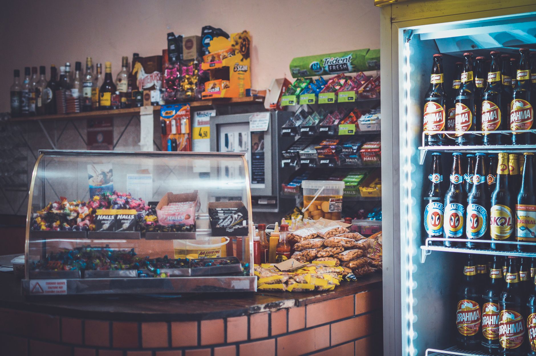 A well stocked convenience store counter with snacks, drinks, and a refrigerator showcasing beverages.