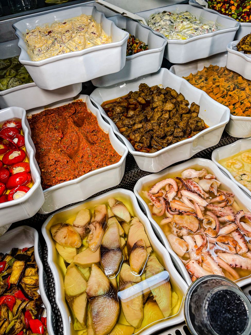 A variety of marinated and prepared foods displayed in white trays at a deli counter.