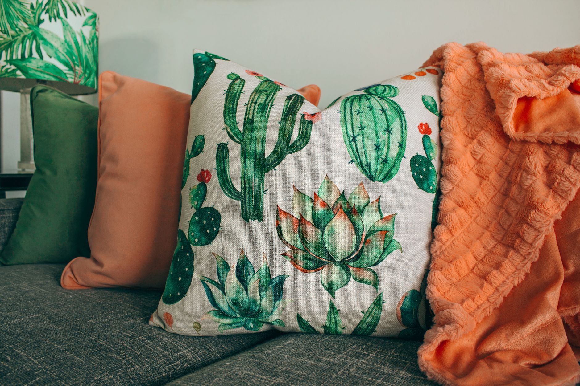 A stylish living room setup with cactus themed pillow and soft orange blanket.
