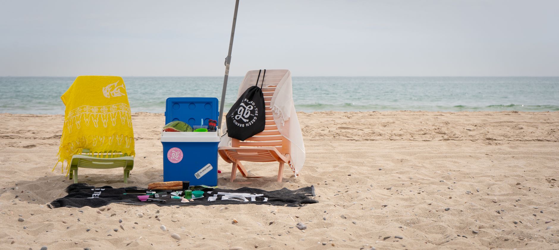 A calm beach scene with chairs, a cooler, and beach towels set for a relaxing day by the ocean.