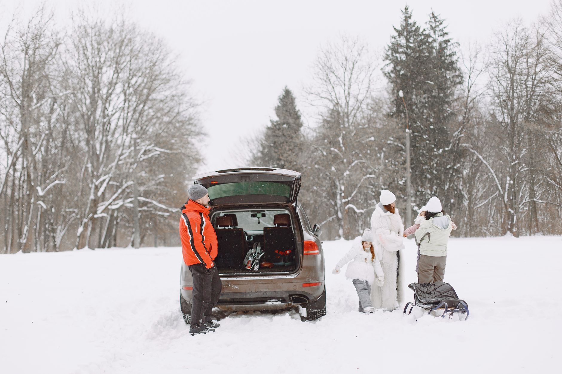 Family in winter gear preparing for outdoor adventure with SUV in snow covered landscape.