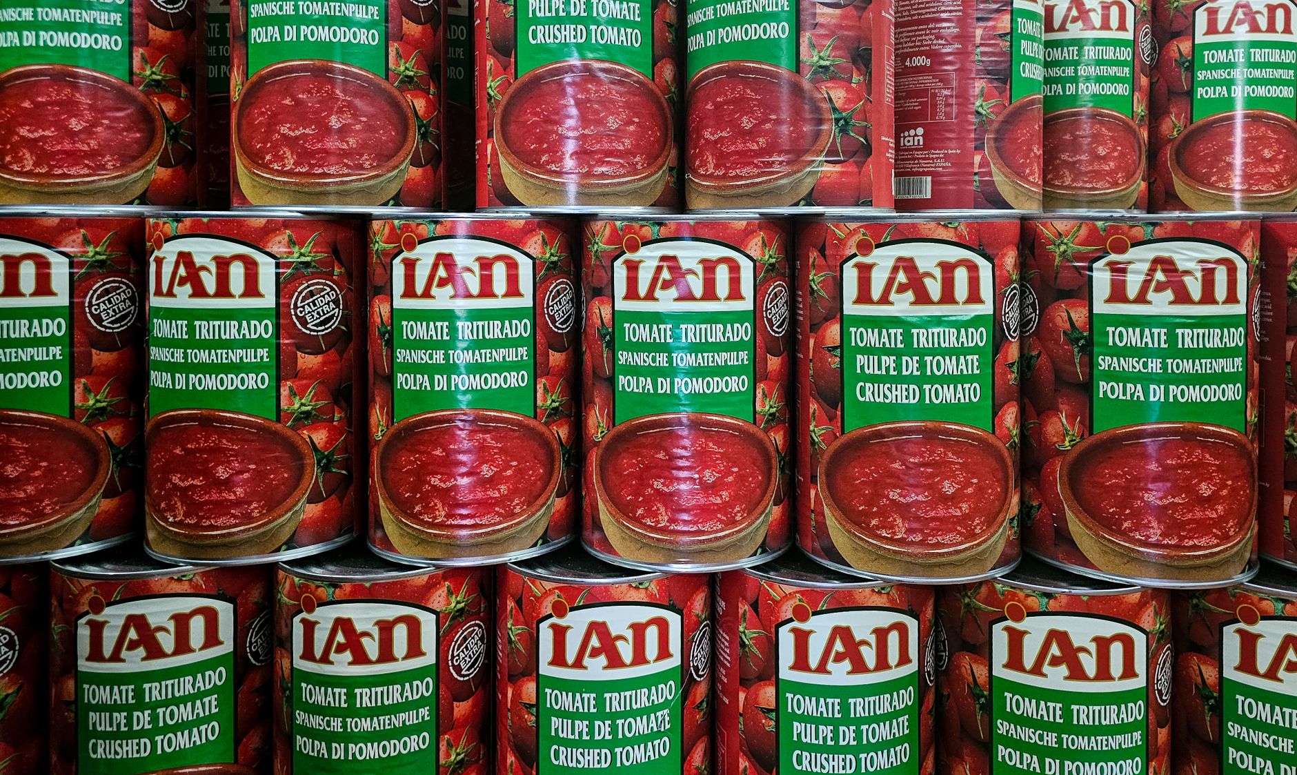 Close up of stacked cans of crushed tomatoes in vibrant red with multilingual labels.