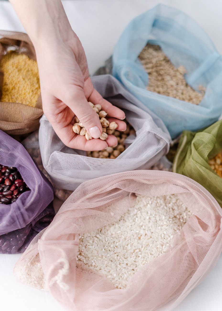 Hand holding chickpeas above colorful reusable bags with grains, promoting zero waste living.