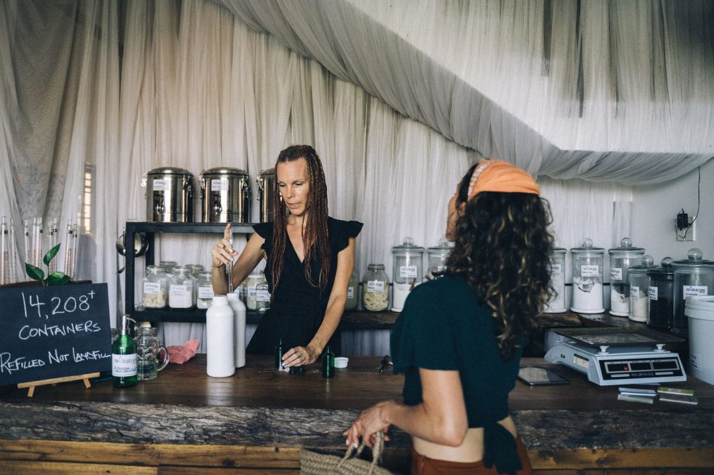 Two women engage at a sustainable refill station with reusable containers.