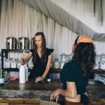 Two women engage at a sustainable refill station with reusable containers.