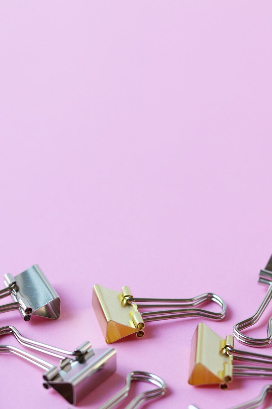 Metallic binder clips scattered on a pastel pink background, ideal for office stationery themes.