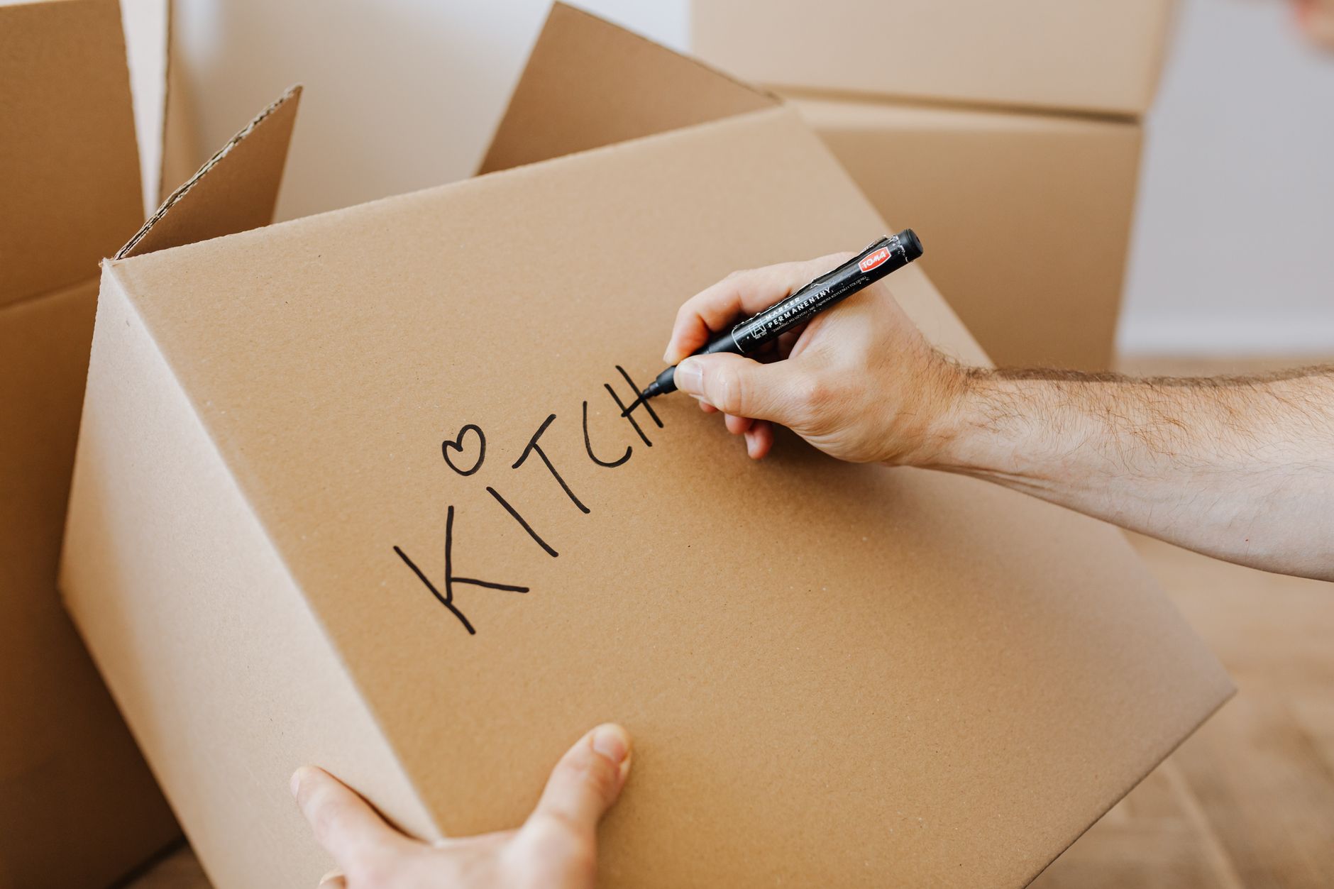 From above of unrecognizable adult male writing with black marker on cardboard containers while packing staff and preparing for relocation in new home