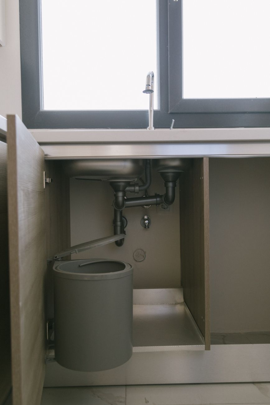 Under sink view of modern plumbing with garbage bin in an Istanbul apartment kitchen.