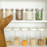 A neat pantry shelf showing various grains stored in labeled glass and plastic containers, promoting kitchen organization.