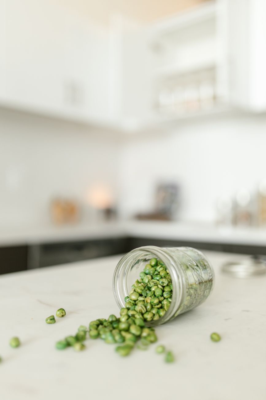 Close up of green beans spilled from a glass jar on a marble top kitchen counter.