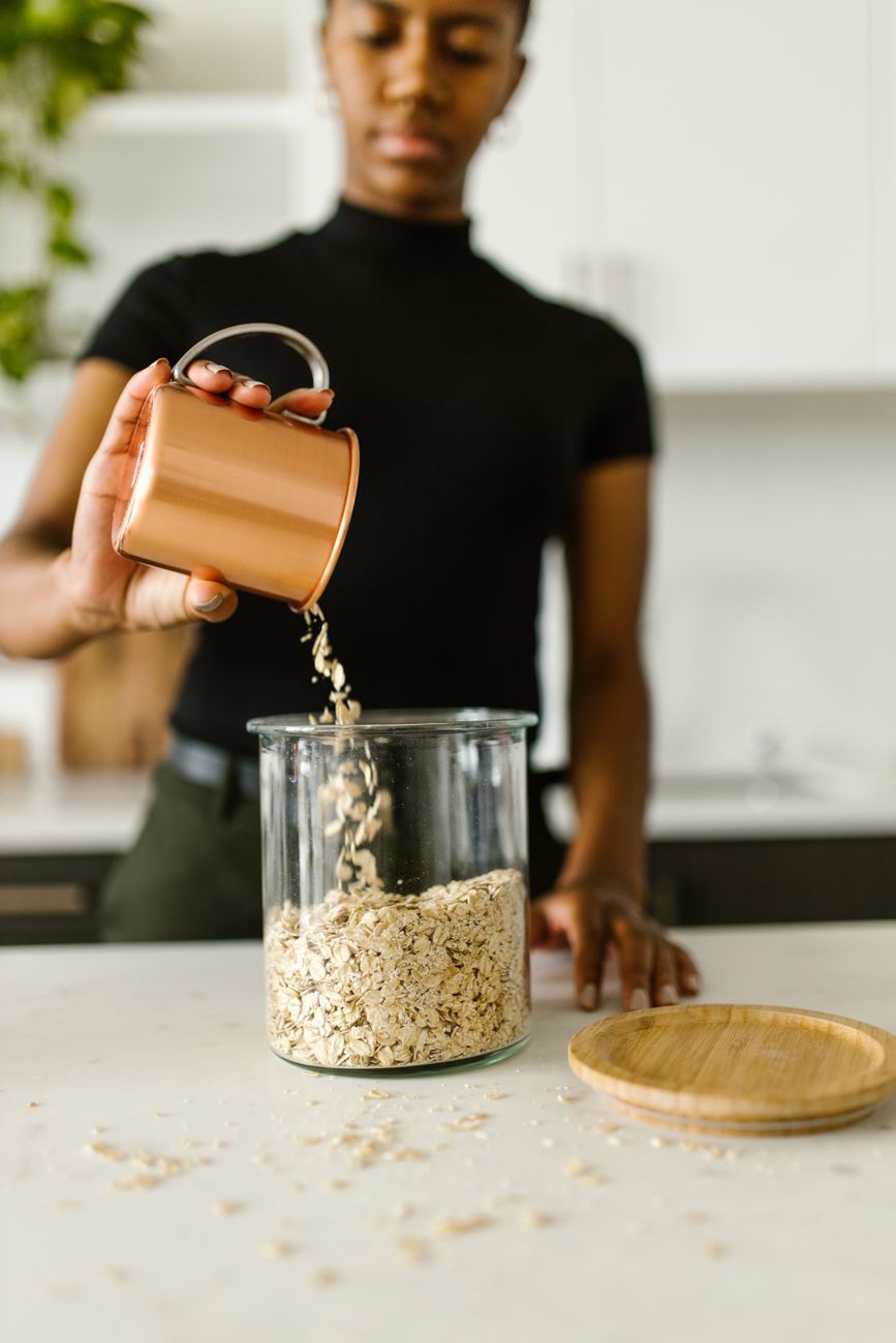 Close up shot of a person pouring oats from a copper mug into a glass jar on a countertop. Perfect for food stock photos.