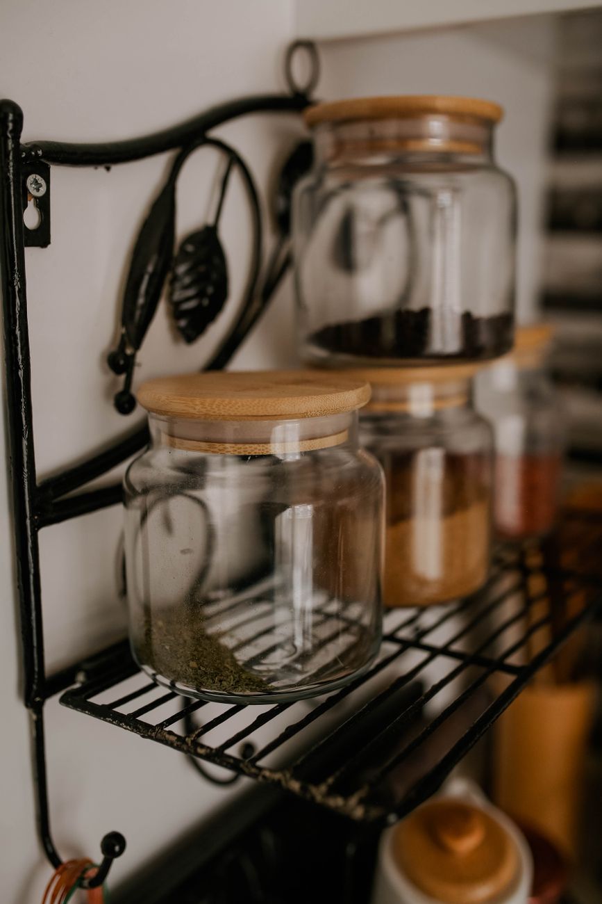 Close up of glass jars with wooden lids on a metal kitchen shelf.