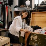 Young woman browsing vintage garments in a cozy thrift shop setting.
