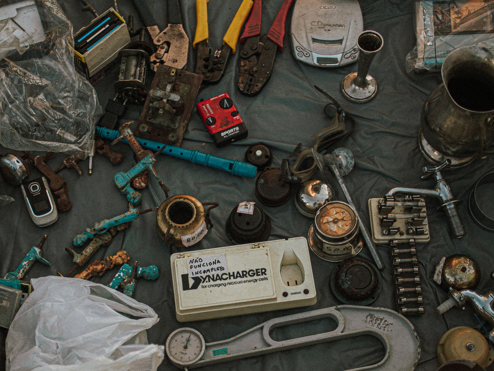Scattered assortment of old metal tools, gadgets, and household items displayed at an outdoor flea market.