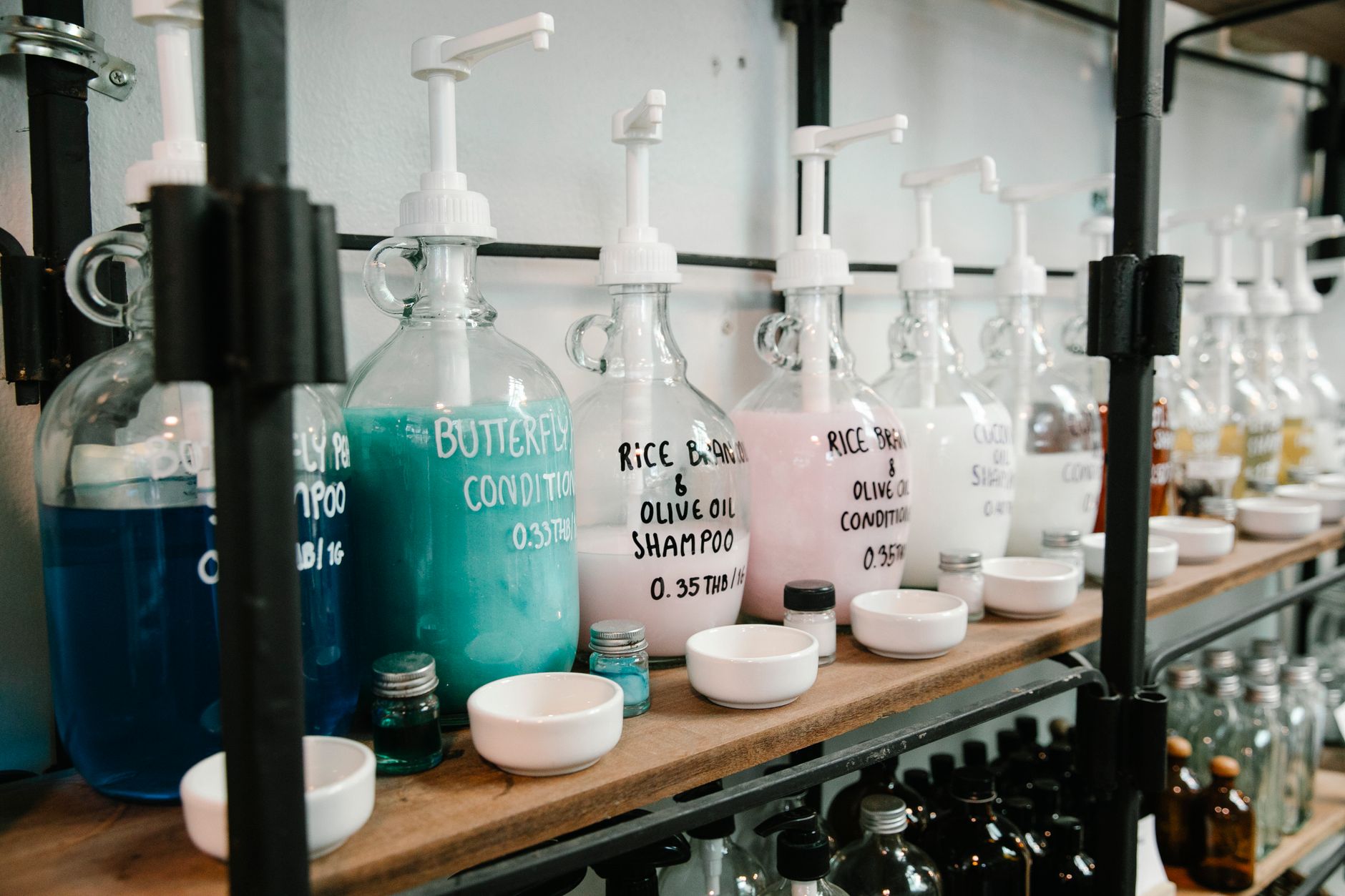 Raw of big marked dispencers with multicolored shampoo with white bowls and glass jars on wooden shelfs