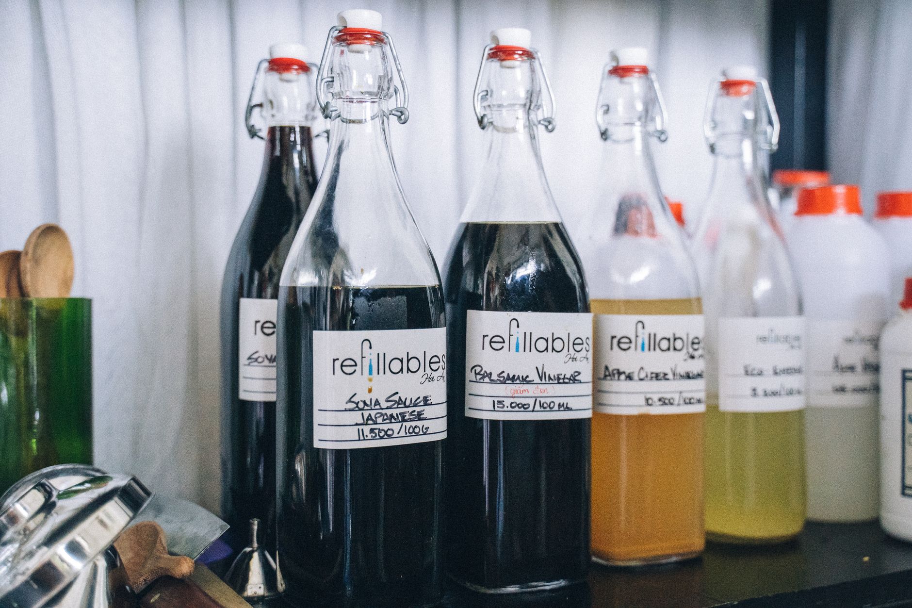 Collection of eco friendly refillable glass bottles for various condiments with labels in a kitchen setting.