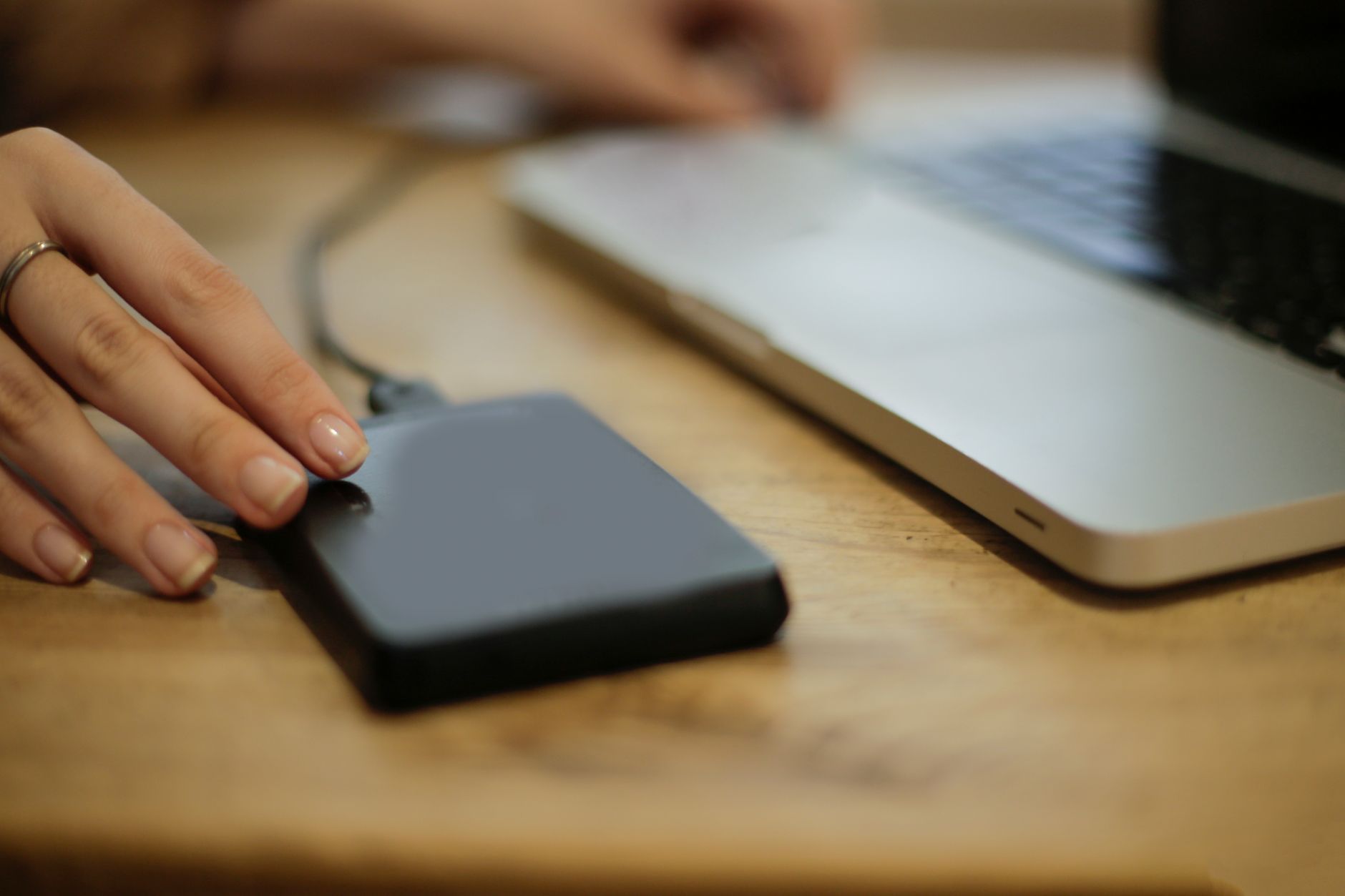 Close up of a person connecting an external hard drive to a laptop on a desk.