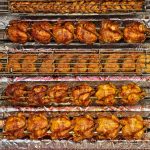 Rows of perfectly cooked rotisserie chickens and grilled meats.