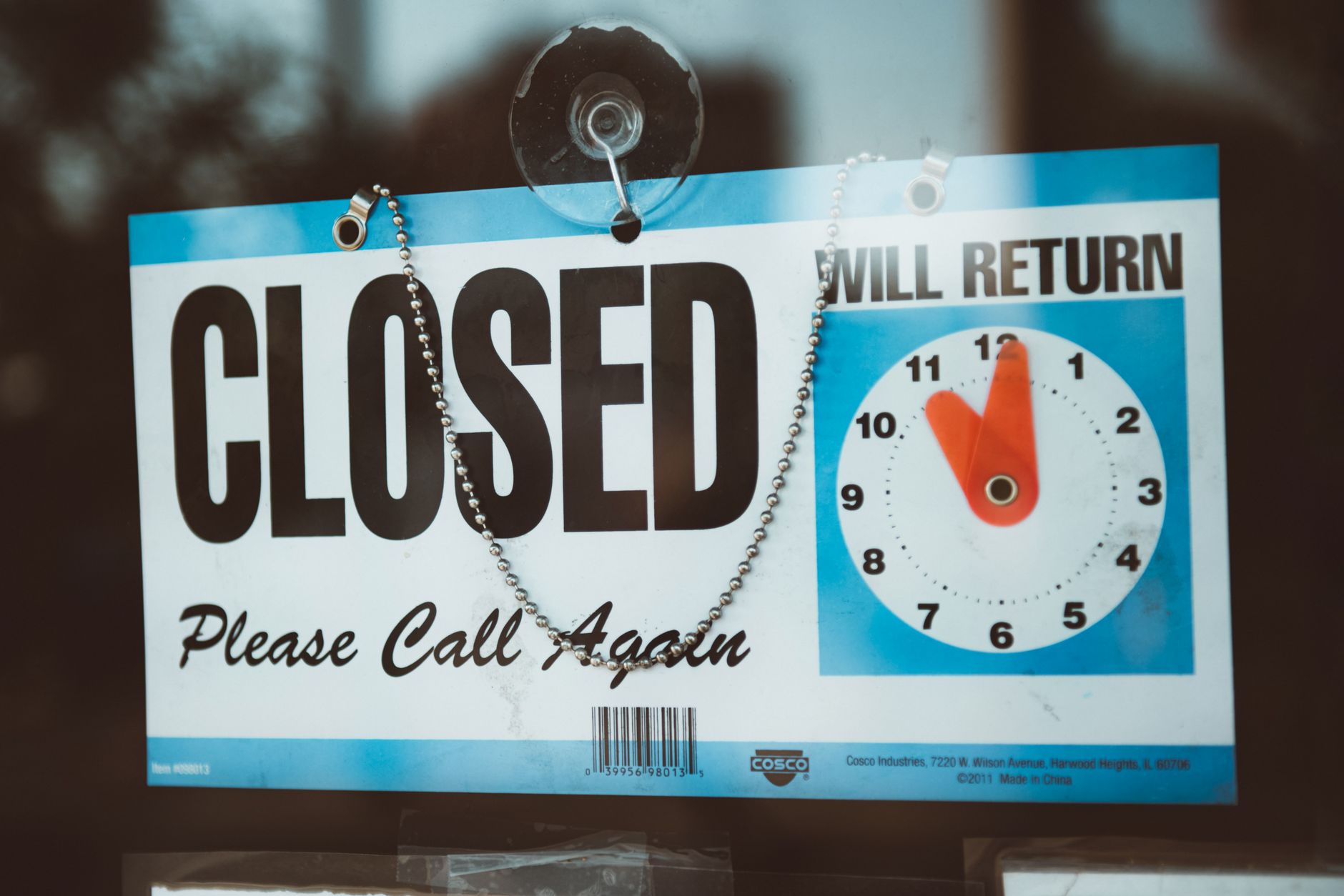 A close up view of a 'Closed' sign on a door, displaying a return time.