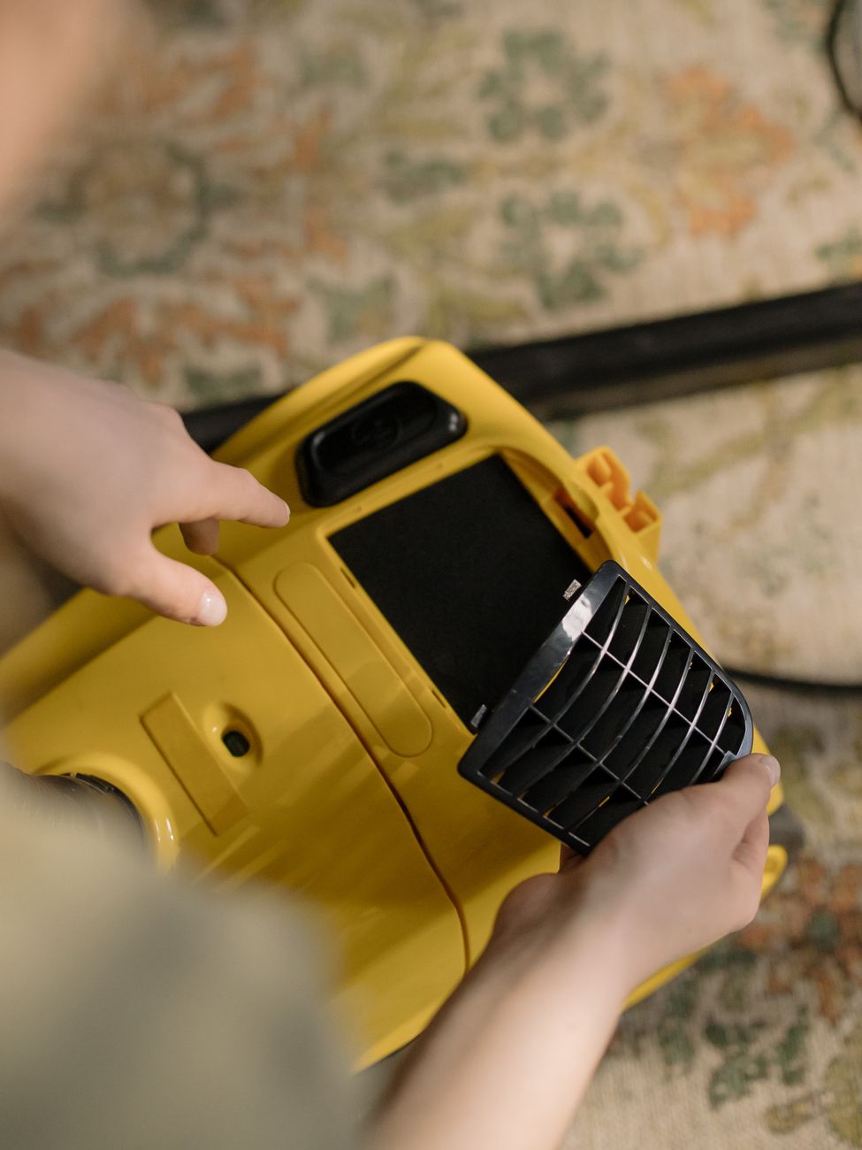 A person is changing the filter of a yellow vacuum cleaner indoors, showing a close up view.
