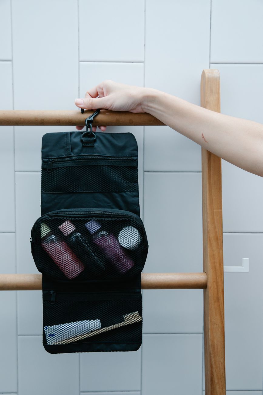 Close up of a toiletry bag hanging on a wooden rack with toiletries.