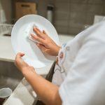 A person cleaning a ceramic plate by hand in a modern kitchen setting.