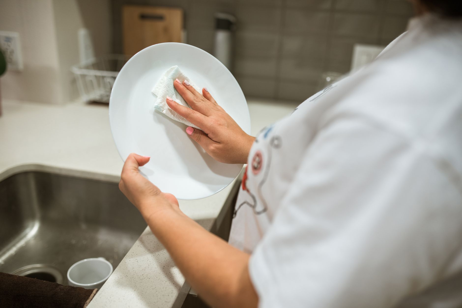 A person cleaning a ceramic plate by hand in a modern kitchen setting.