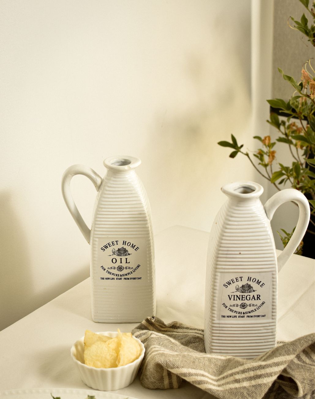 Stylish ceramic oil and vinegar bottles on a kitchen tabletop in a bright, rustic setting.