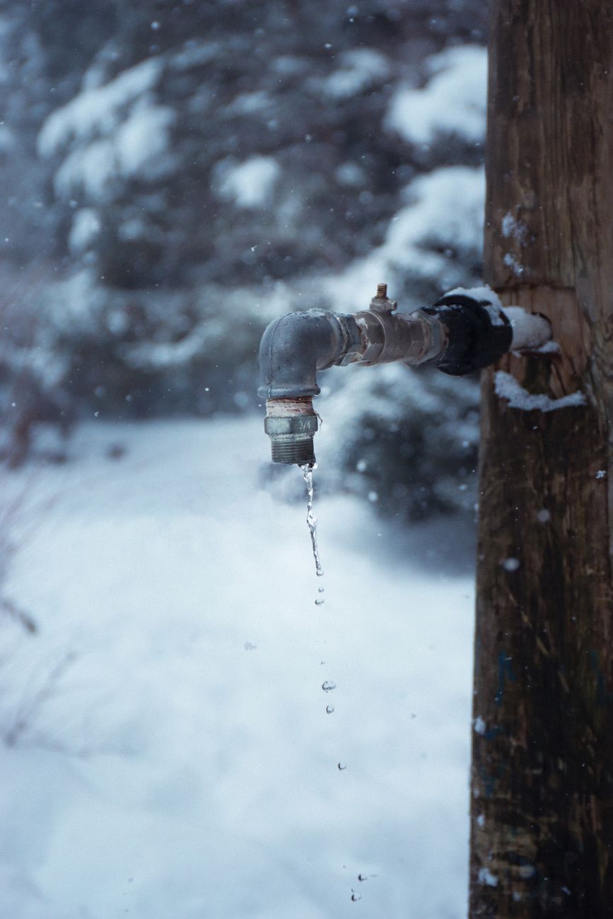 Close up of a frozen water tap dripping outdoors in a snowy winter landscape.