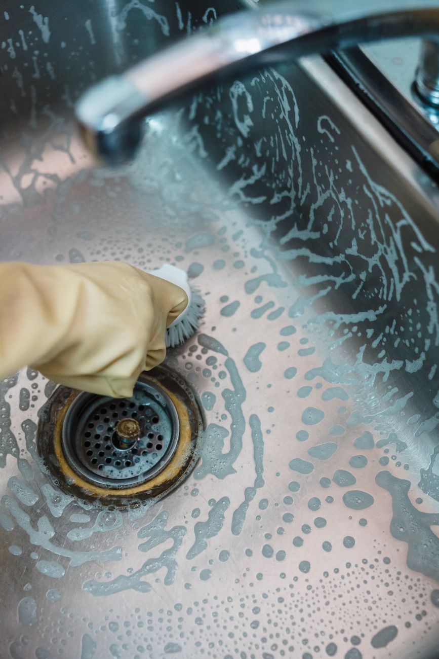Close up of a hand cleaning a soapy stainless steel sink using a brush.