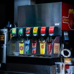 Soft drink dispenser with various soda options in fast food restaurant.