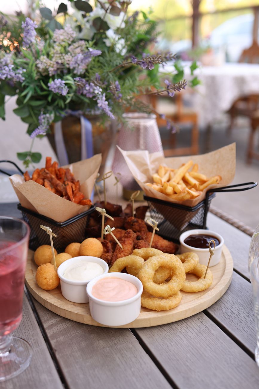 Close up of a diverse fried snack platter with dips, served outdoors with floral decor in the background.