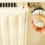 Close up of hand adjusting radiator thermostat to control home heating temperature.
