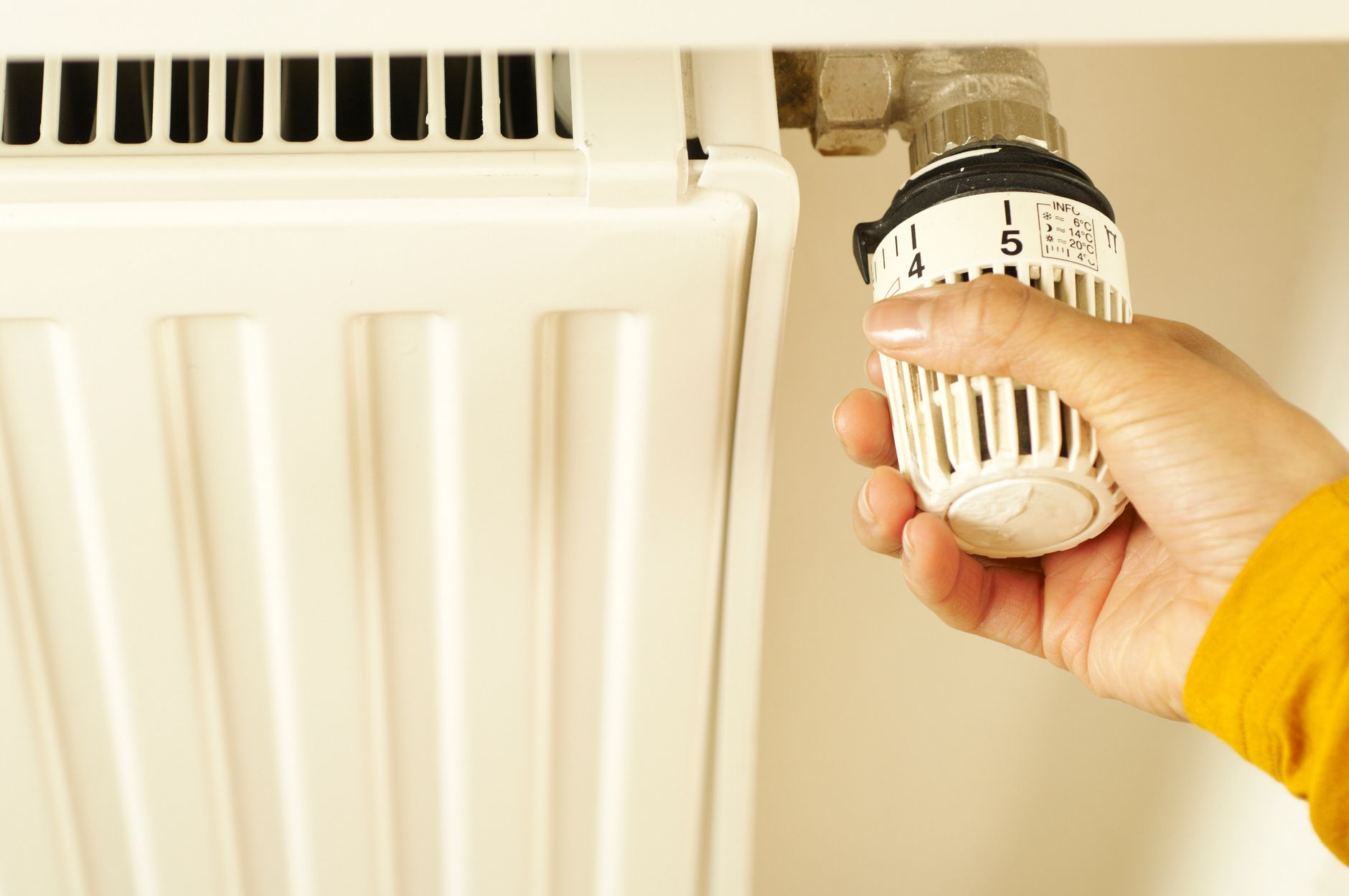 Close up of hand adjusting radiator thermostat to control home heating temperature.