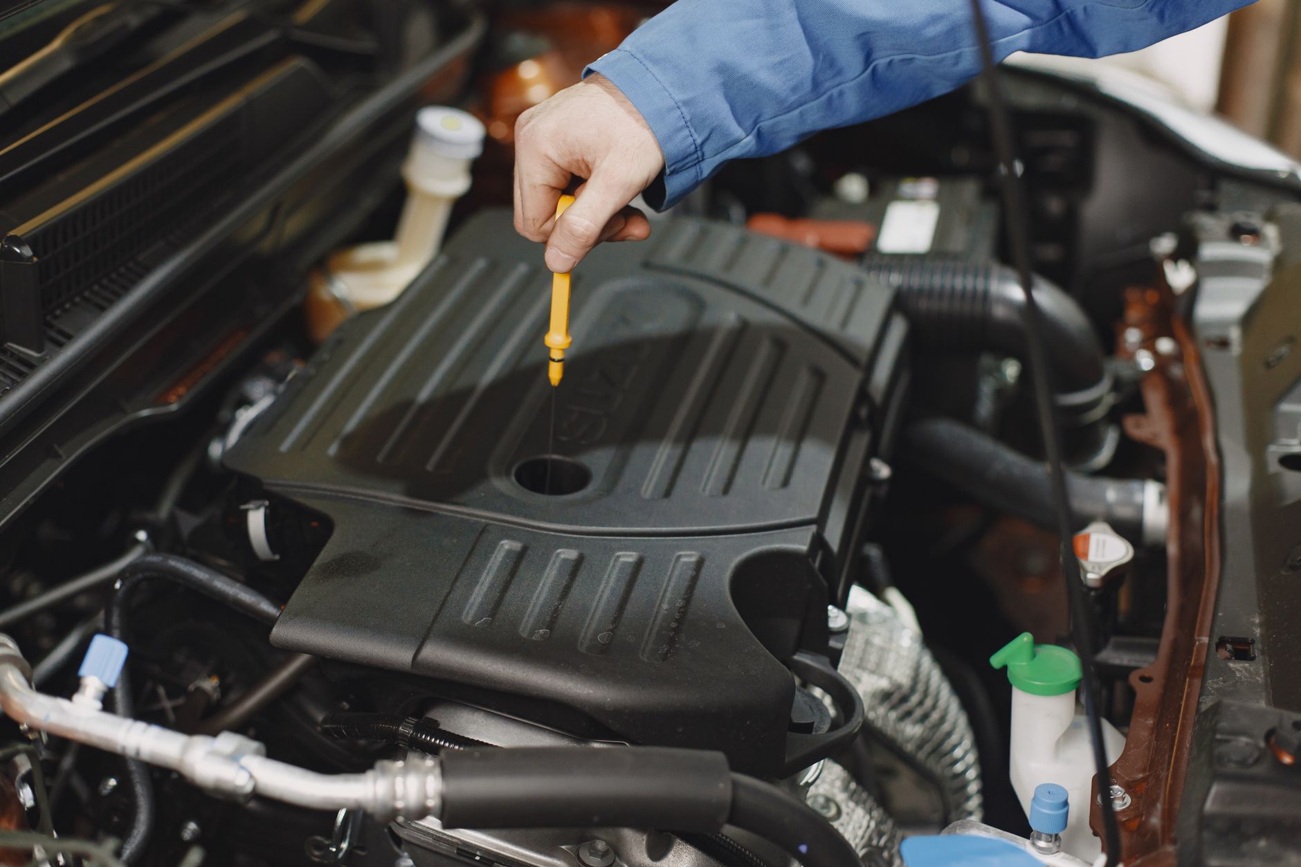 Close up of a person checking engine oil using a dipstick in a car's engine bay.