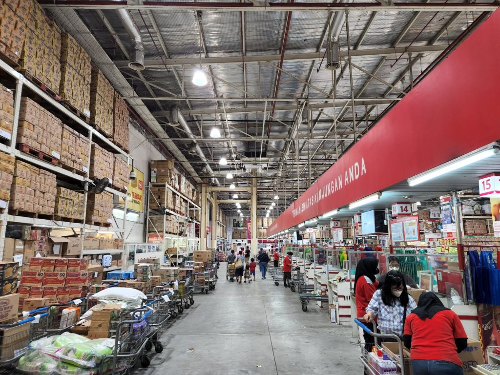 Vibrant warehouse scene showcasing rows of stocked shelves and busy shoppers with carts.