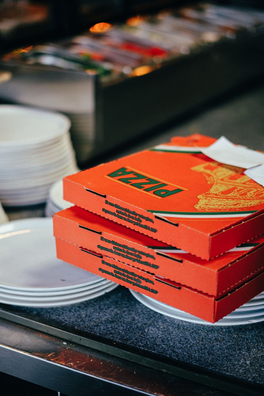 Close up of stacked pizza boxes on a countertop with plates, ready for serving.